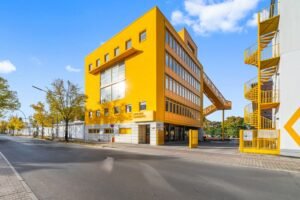 The eye-catching modern building "ATELIER CHARLEMAGNE" features large windows, a yellow open-air corridor and a spiral staircase connecting to the white building.
