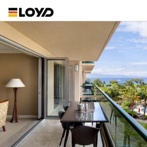 ELOYD balcony with a dark wood dining set, wine bottle and glasses, overlooking a tropical view of the sea, palm trees, and blue sky through a large glass door.