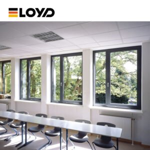 A bright and modern classroom with large ELOYD windows offering views of green trees, featuring white study tables, black and wood chairs, and ample natural light.