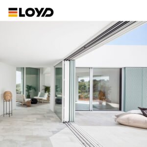 Modern interior by ELOYD with large white folding glass doors opening to a garden, featuring marble floors, a chair, and floor cushions.