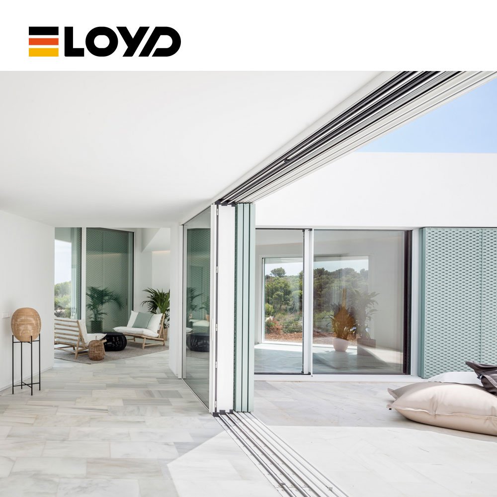 Modern interior by ELOYD with large white folding glass doors opening to a garden, featuring marble floors, a chair, and floor cushions.