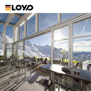 Upscale mountain restaurant interior by ELOYD featuring dark wood tables, metal barstools, and expansive floor-to-ceiling windows framing a breathtaking view of snow-covered peaks under a blue sky.