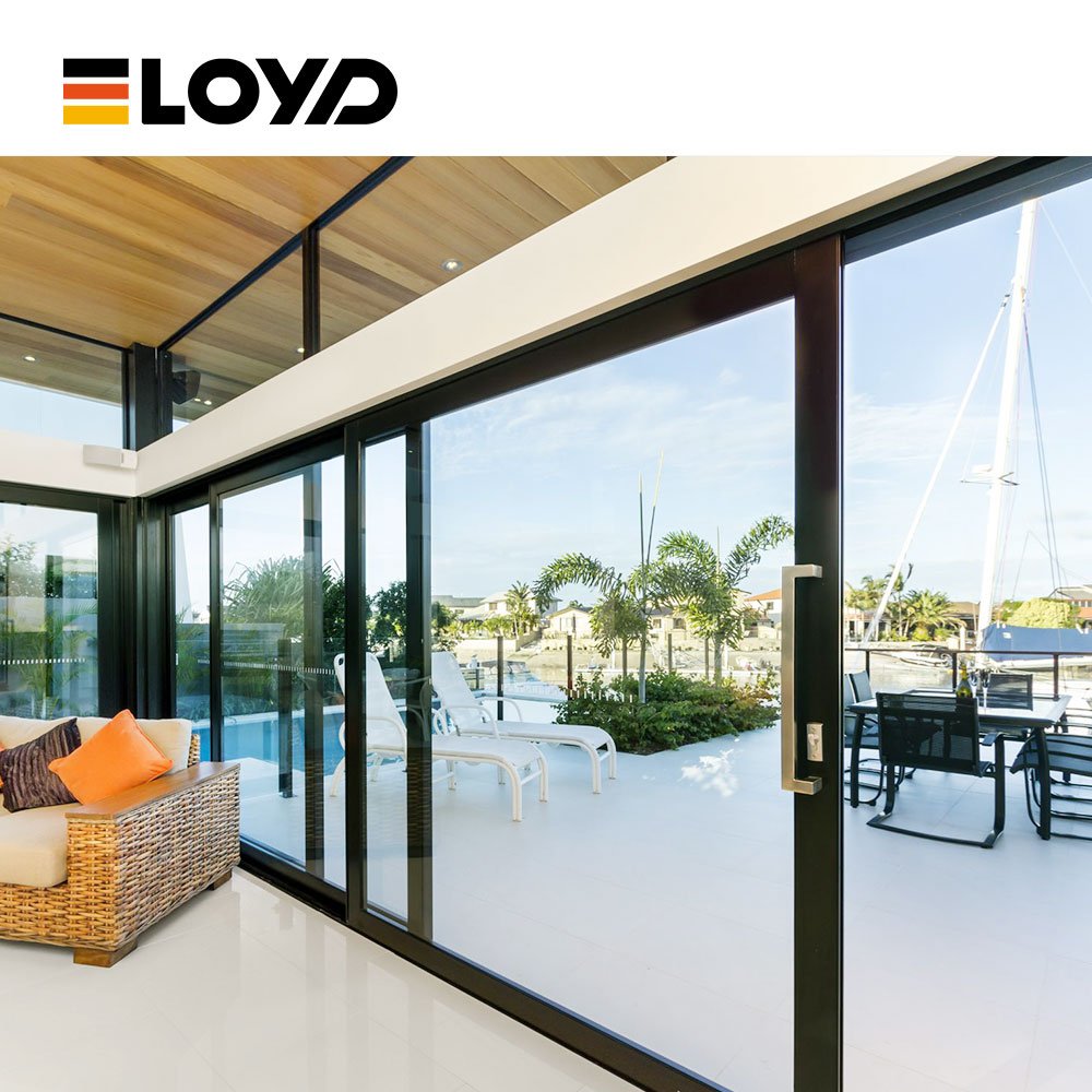 ELOYD modern living area with large black sliding glass doors opening to a patio with palm trees and sea view, featuring a rattan sofa and wooden ceiling.