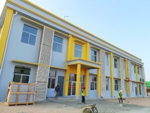 Construction workers in safety gear laying pavement in front of a new modern two-story ELOYD house with grey walls, yellow accents, and multiple windows.